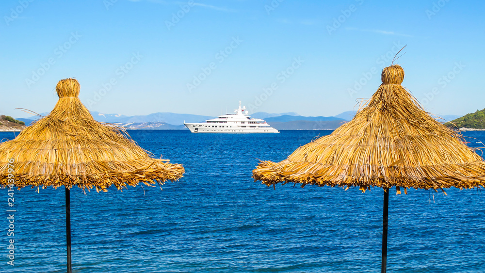 Blue sea with a white boat and straw umbrellas on the beach Blue sea with a white boat and straw umbrellas on the beach