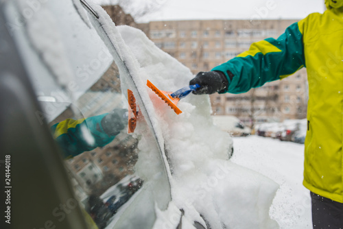 man with scrapper cleaning car out of snow