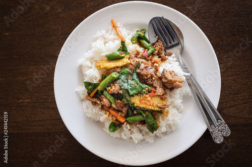 Rice topped with stir fried beef and basil. Put the dish white. on the table Brown