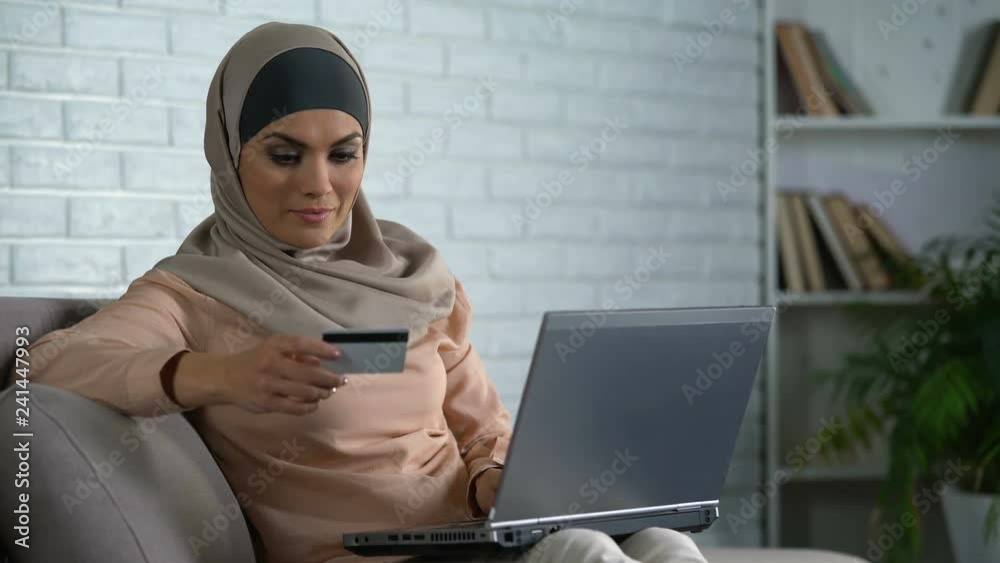 Modern arab housewife typing card number on laptop, banking online, purchase Modern arab housewife typing card number on laptop, banking online, purchase