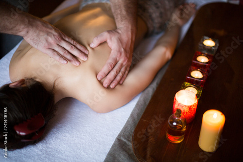 Male hands massaging female back. candles on background. Healthcare and relax concept