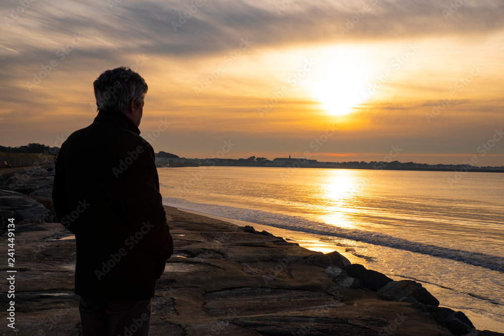A man looks at the horizon in front of the sea and a sunset