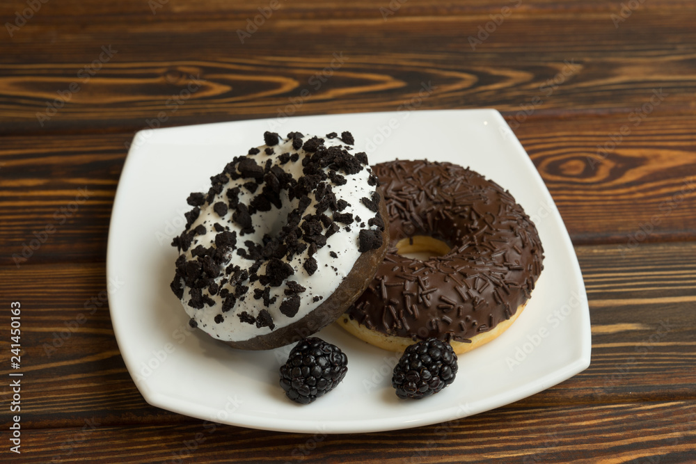 Chocolate donuts with icing and blackberries lie on a plate Chocolate donuts with icing and blackberries lie on a plate