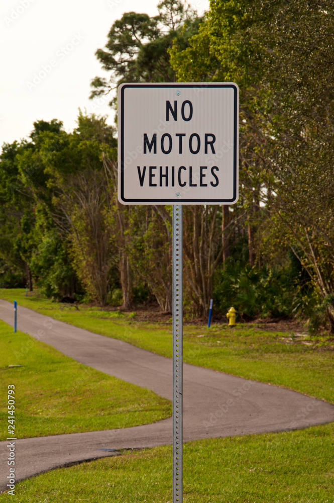 Vertical image of a no motor vehicles sign at base of an empty walking trail/ bike path in bonita springs florida. Vertical image of a no motor vehicles sign at base of an empty walking trail/ bike path in bonita springs florida.