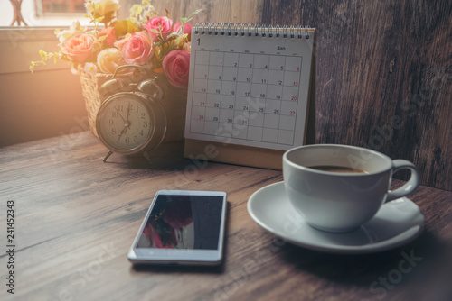 Working space at home, Cup of Coffee with Calendar 2021, smartphone, clock and pot of rose flower on blue wooden desk. Urban Lifestyle concept