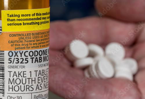 Oxycodone is the generic name for opoid pain killing tablets. Prescription bottle for Oxycodone tablets with hand holding drugs