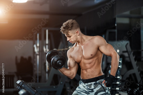 Muscular young man lifting weights on dark background
