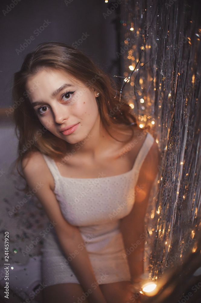 delicate and beautiful young girl in white dress on the background of garlands and tinsel delicate and beautiful young girl in white dress on the background of garlands and tinsel