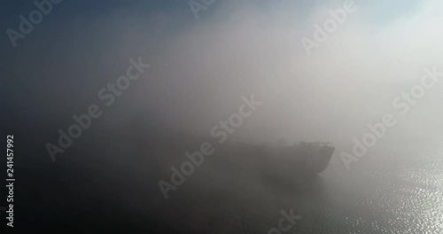 A huge barge on the river Dnipro in the morning fog with a visible silhouette of the buildings and city in the background (shot from the air) in 4K 6