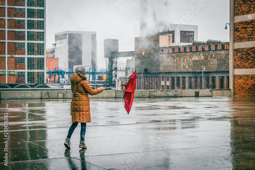 Φωτογραφία Woman with red umbrella is walking in idustrial city during blizzard