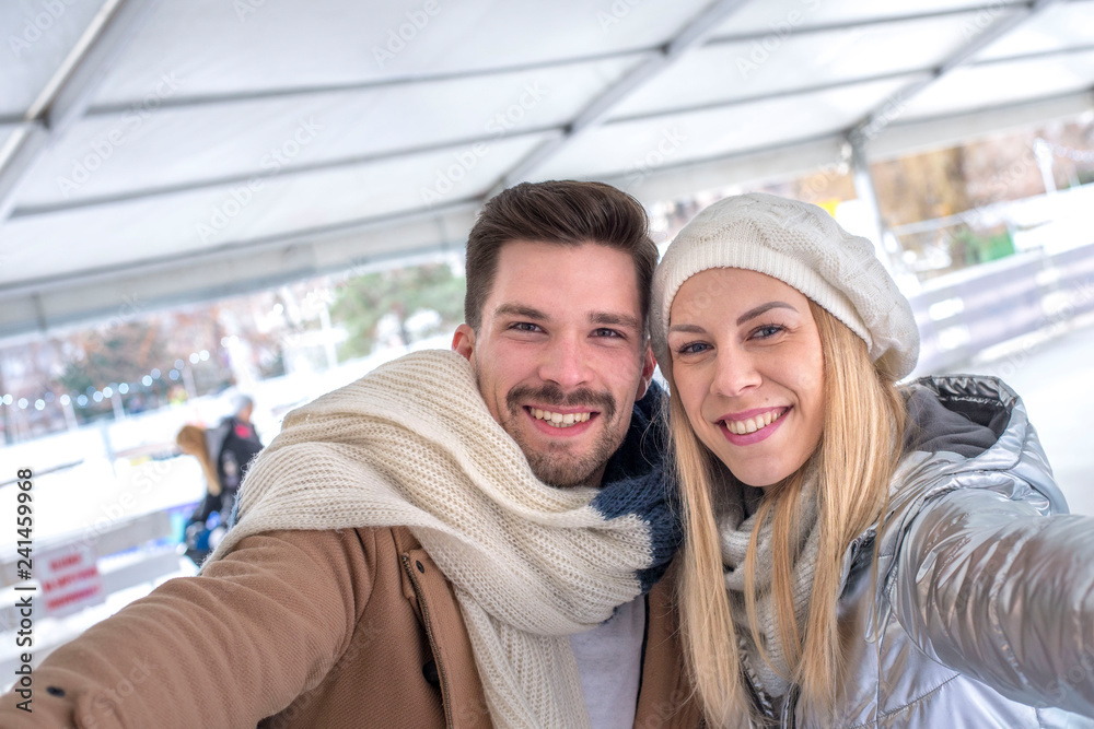 Happy smiling couple having fun on the ice rink while making selfie photo and spending time together