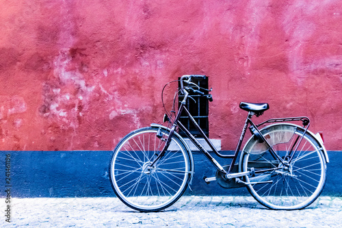 Black bicycle near a red and blue painted wall with a small window photo