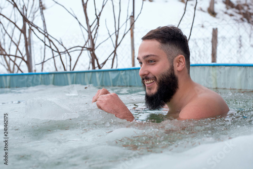 Young smiling man having fun while swimming in an ice hole in a winter day © Drpixel