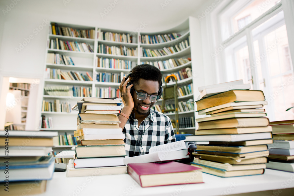 Young man student reading book for exam and listening to music with headphones in library at the university,Concept of education and reading Young man student reading book for exam and listening to music with headphones in library at the university,Concept of education and reading