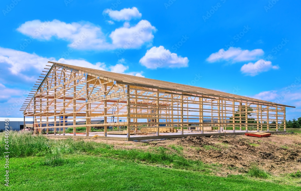 New pole barn showing wood framing, being built on a concrete slab. Blue sky is in the background.