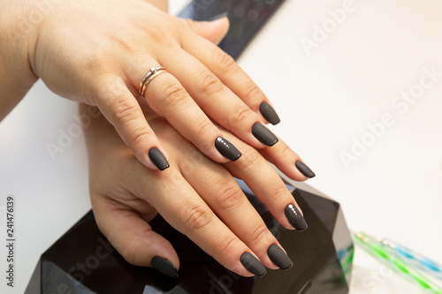 Female hands with a beautiful manicure  the master in the salon varnishes nails  close-up