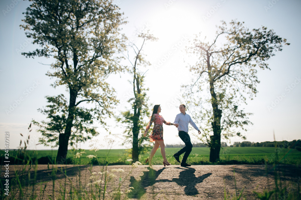Beautiful young couple holding hands and running in sunshine in spring field and trees. Silhouettes of happy family having fun  in sunlight. Romantic joyful moments. Space for text