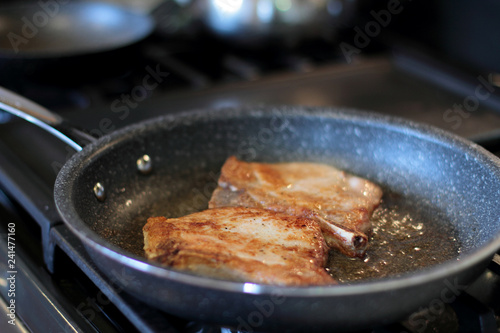 Pork chops frying in a pan on a stove top. 
