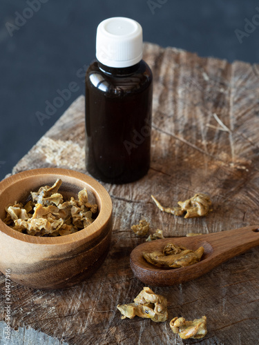 A bottle of propolis and wooden bowl and spoon of propolis granules on piece of wood.