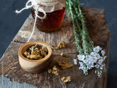 Jar of honey, flowers and wooden bowl and spoon of propolis granules on piece of wood.