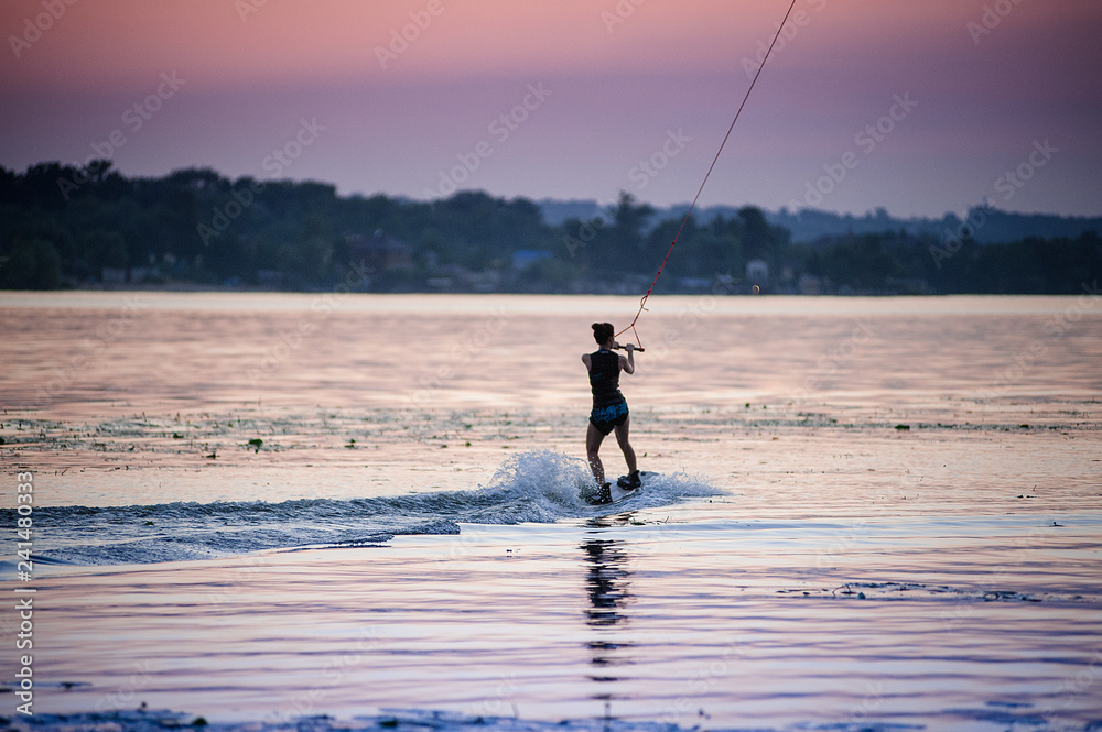 Girl riding on Wakeboarding on sunset. splashes of water