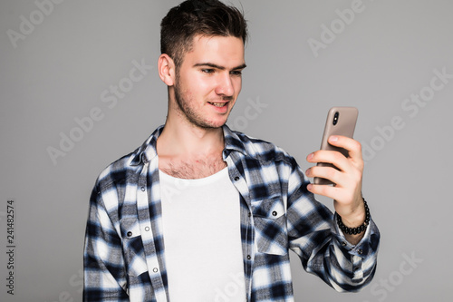Portrait of a joyful man in white shirt using mobile phone while standing isolated over gray background © F8  \ Suport Ukraine