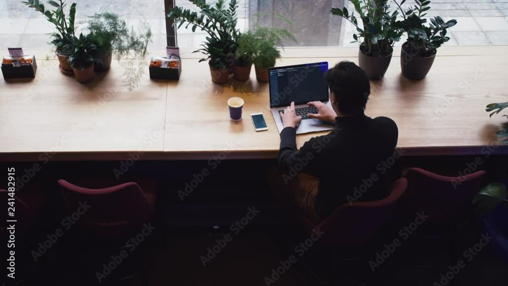 Top view of mixed race man working with laptop and smart phone at cafe. Plants at background. Top view of mixed race man working with laptop and smart phone at cafe. Plants at background.