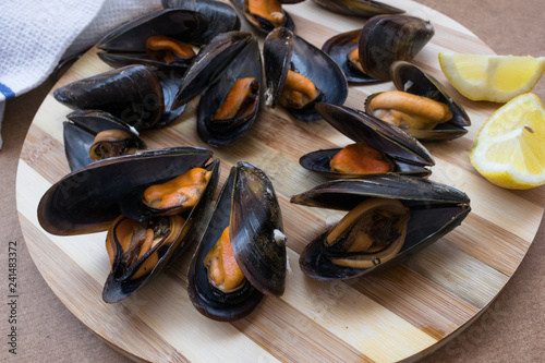 delicious steamed mussels ready to eat together with half a lemon on a wooden plate