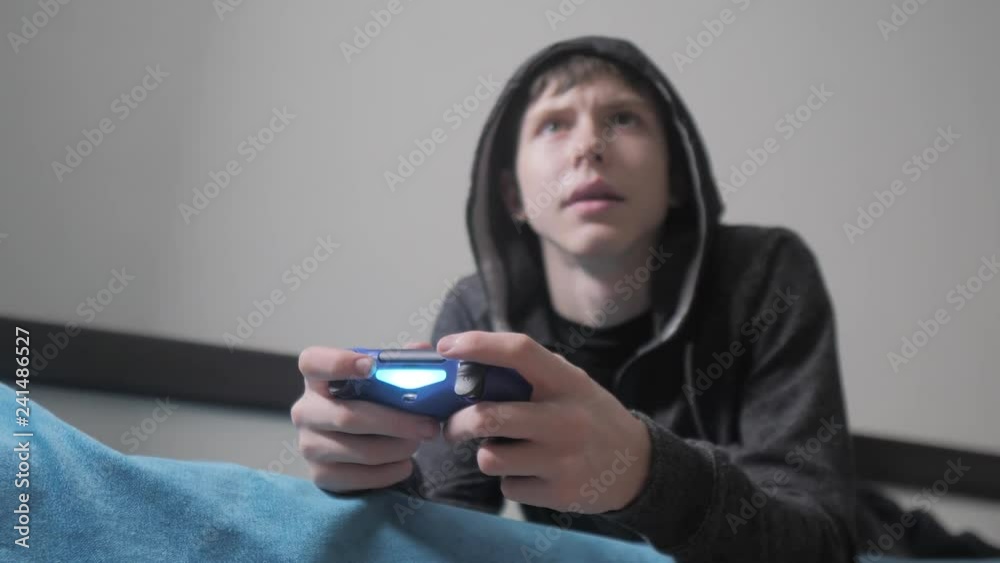 young teen and joystick man cybersport hooded sweater absorbed In online video game. boy teenager in the hood playing video games on the console on the gamepad. Controller console gamepad. Gaming man young teen and joystick man cybersport hooded sweater absorbed In online video game. boy teenager in the hood playing video games on the console on the gamepad. Controller console gamepad. Gaming man