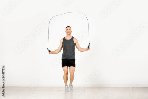 Full length portrait of young sportive man training with jump rope in light room © New Africa