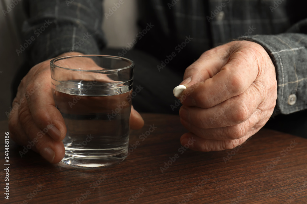 Senior man holding pill and glass of water at table, closeup Senior man holding pill and glass of water at table, closeup