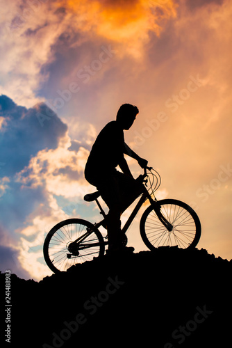 Fototapeta Naklejka Na Ścianę i Meble -  Silhouette of a boy riding a mountain bike at sunset