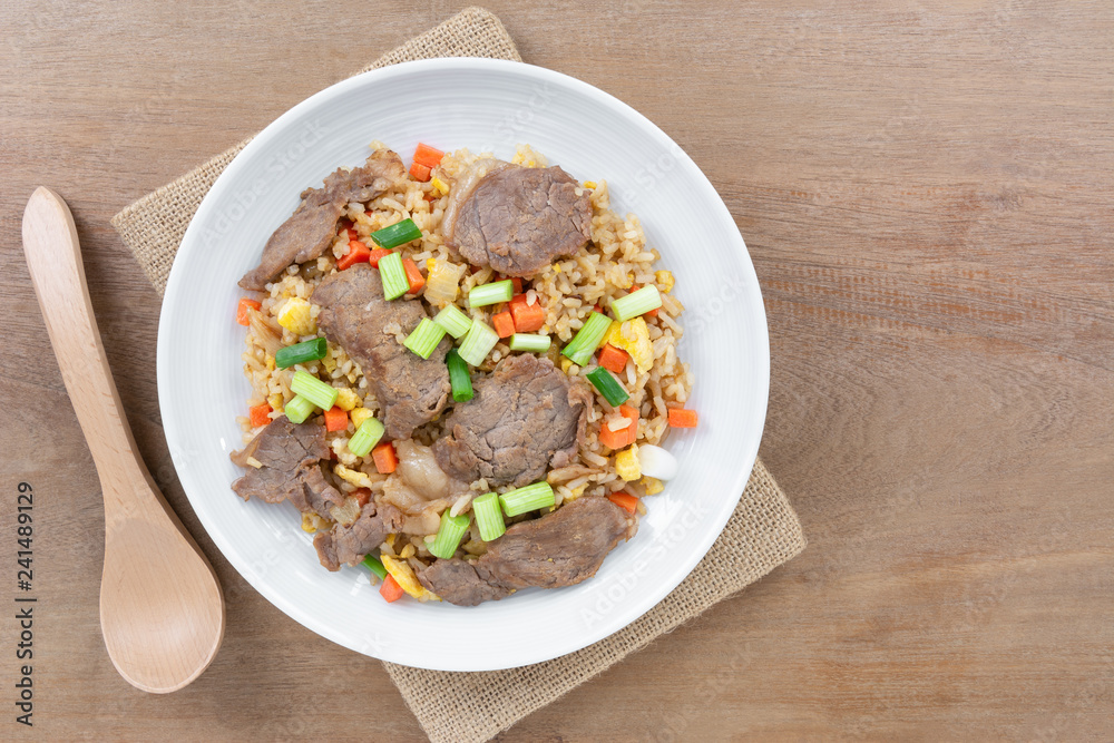 top view of fried rice with beef in a ceramic dish on wooden table. asian homemade style food concept.