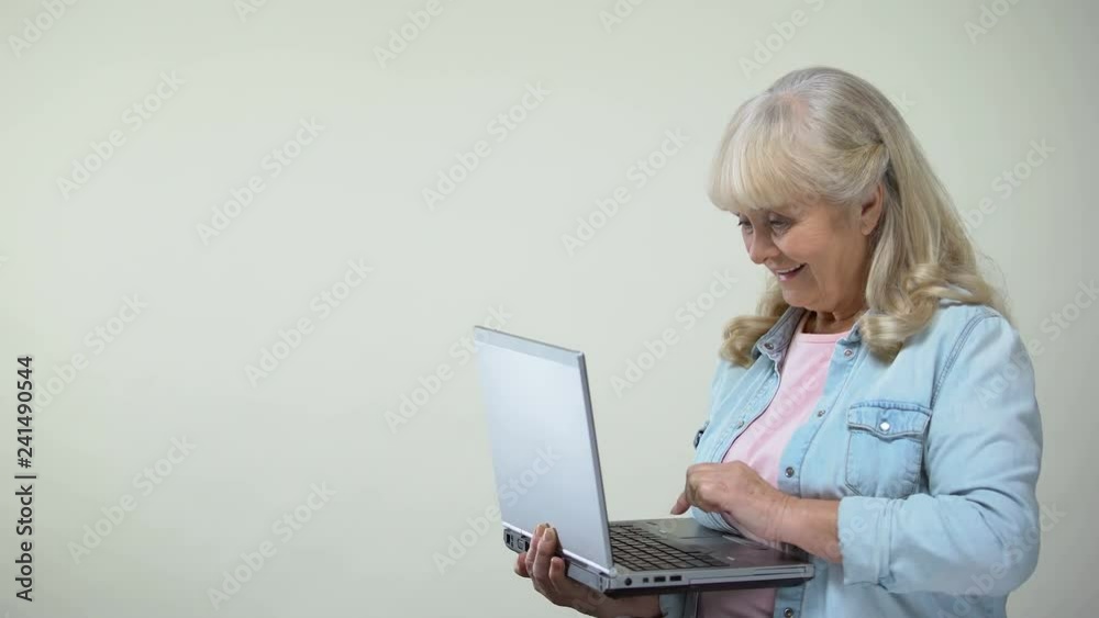 Aged lady typing on laptop showing thumbs-up, computer literacy for retirees Aged lady typing on laptop showing thumbs-up, computer literacy for retirees