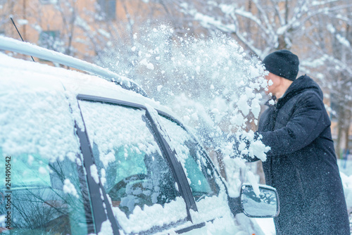 adult male removing snow from car roof with brush in winter season