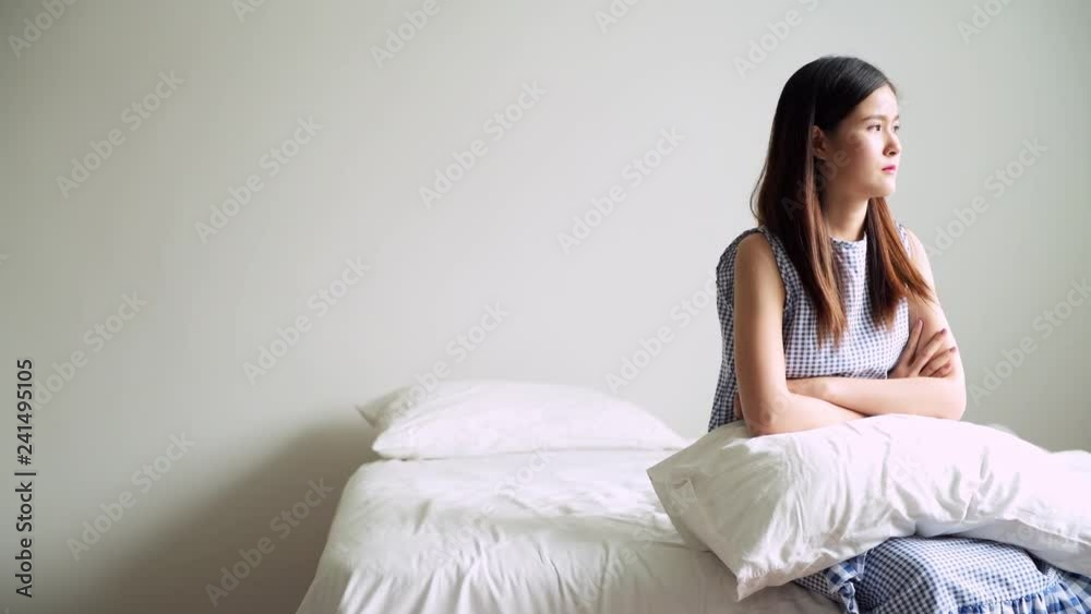 Young asian woman sitting in bed side looking out the window, feeling unhappy. Young depression medical issue concept. 
