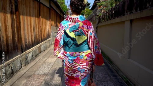 back view of young local woman walking in old town path wearing floral kimono costume going home. japanese lady in traditional costume lifestyle join festival passing through wooden wall in street. photo