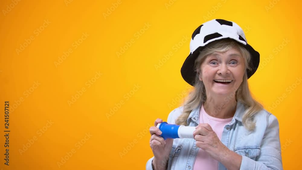 Joyful elderly lady in football fan hat blowing horn, sport betting, active life Joyful elderly lady in football fan hat blowing horn, sport betting, active life