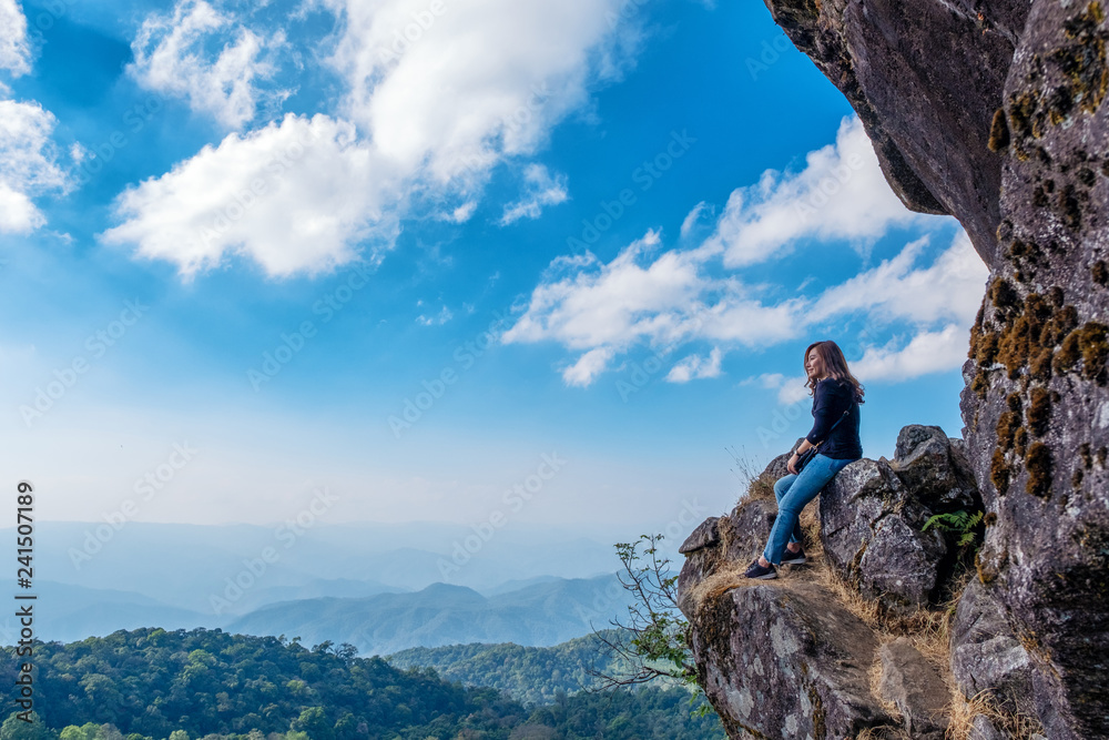 A beautiful asian woman sitting on a cliff with mountains view and blue sky background A beautiful asian woman sitting on a cliff with mountains view and blue sky background