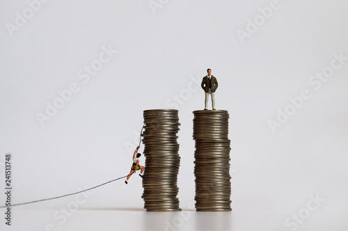 Miniature people with a pile of coins. The concept of income and gender inequality.