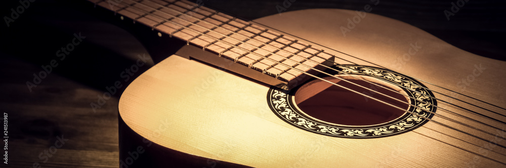 Fototapeta premium Acoustic guitar lying on a wooden table lit by a beam of light.