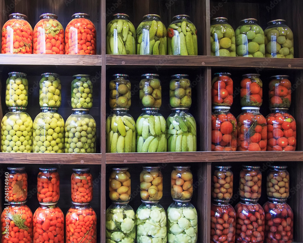 Many glass bottles with preserved food in wooden cabinet.