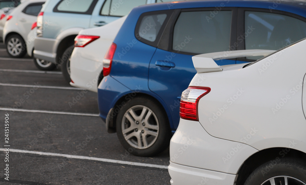 Closeup of rear or back side of white car with other cars parking in parking area in twilight evening. 