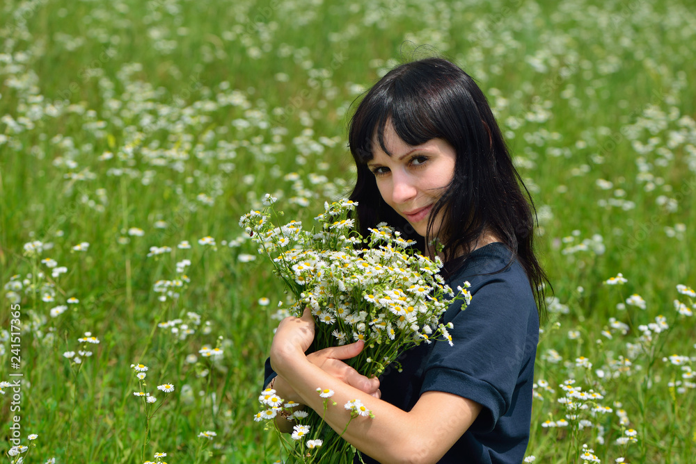 Fototapeta premium The beautiful girl in the field collect a bouquet of camomiles