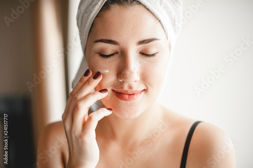 Portrait of a young woman who applies nourishing cream with her hand on her face. Skin care