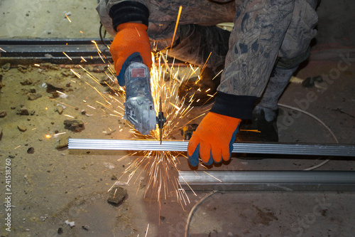 hands of the worker in gloves cut metal profile with a grinding machine. orange sparks fly from the grinding machine while cutting iron.