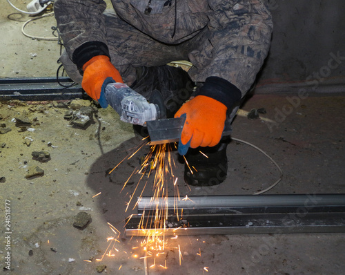  hands of the worker in gloves cut metal profile with a grinding machine. orange sparks fly from the grinding machine while cutting iron.