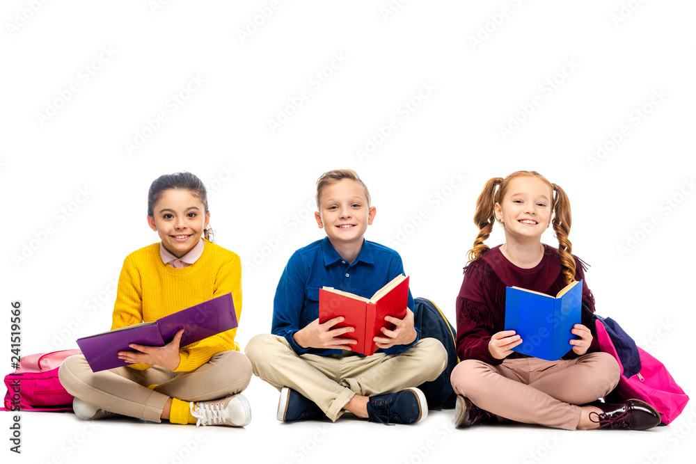 cheerful schoolchildren sitting, holding books and looking at camera isolated on white cheerful schoolchildren sitting, holding books and looking at camera isolated on white