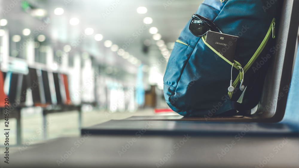 Fototapeta premium Close up passport with headphones and glasses in blue backpack on seat in the interior of airport terminal. Travel concept.