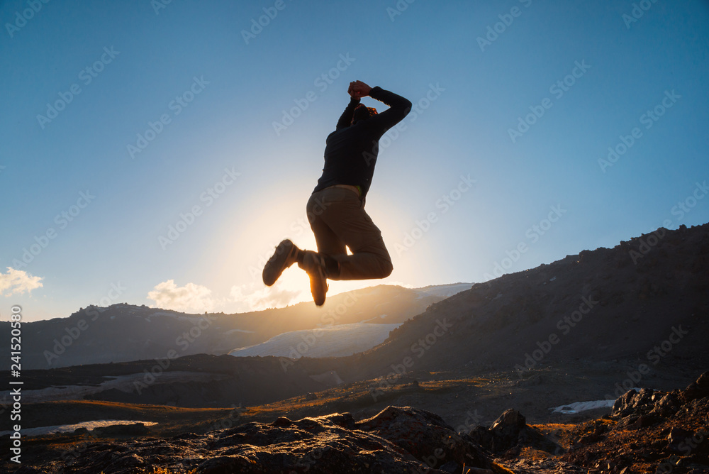 Man jumps on the top of mountain in sun beams. Leadership concept